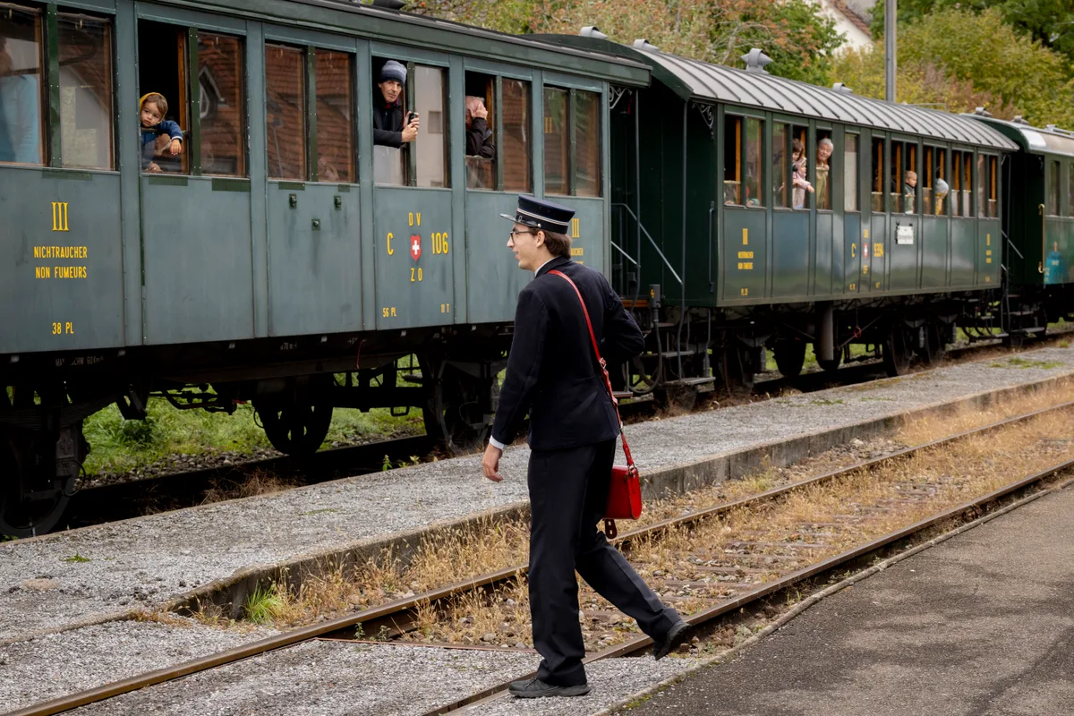 Auch die passende Unform des Bahnschaffners durfte selbstverständlich nicht fehlen. Ein Zugschaffner vor einem alten Zug auf den Gleisen.